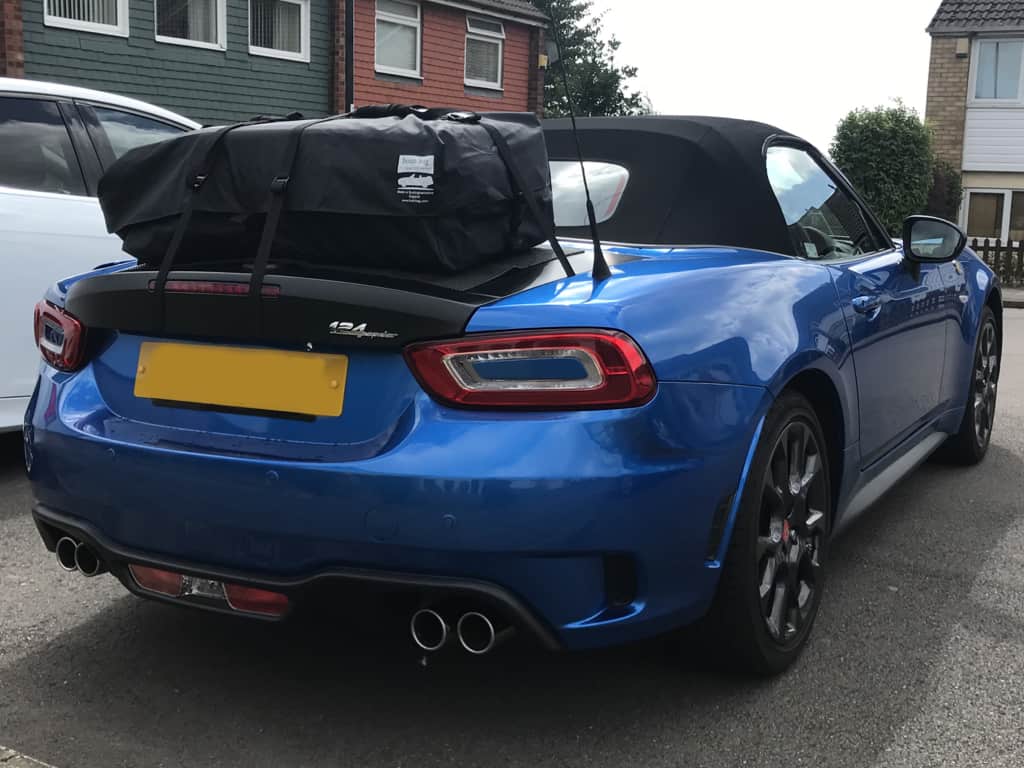 blue fiat 124 spider with a boot-bag vacation luggage rack fitted on a drive / residential road