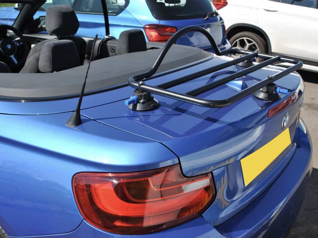 side view of a blue bmw 2 series convertible with the hood down and a black luggage rack fitted to the boot