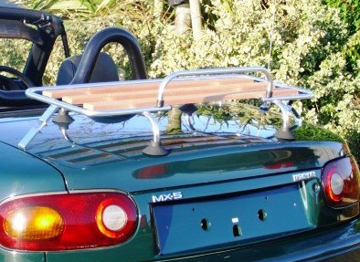 british racing green mazda mx5 mk1 with a wood and chrome luggage rack fitted to the boot next to a hedge