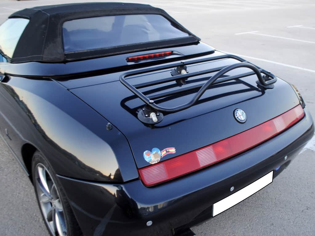 black alfa romeo spider 916 with the hood up and a black luggage rack fitted in a car park