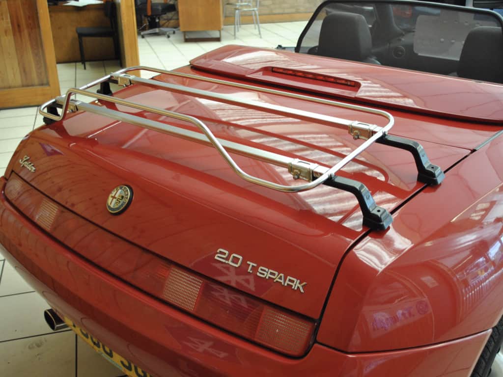 side view of a red 916 alfa spider with the hood down and a luggage rack fitted to the boot
