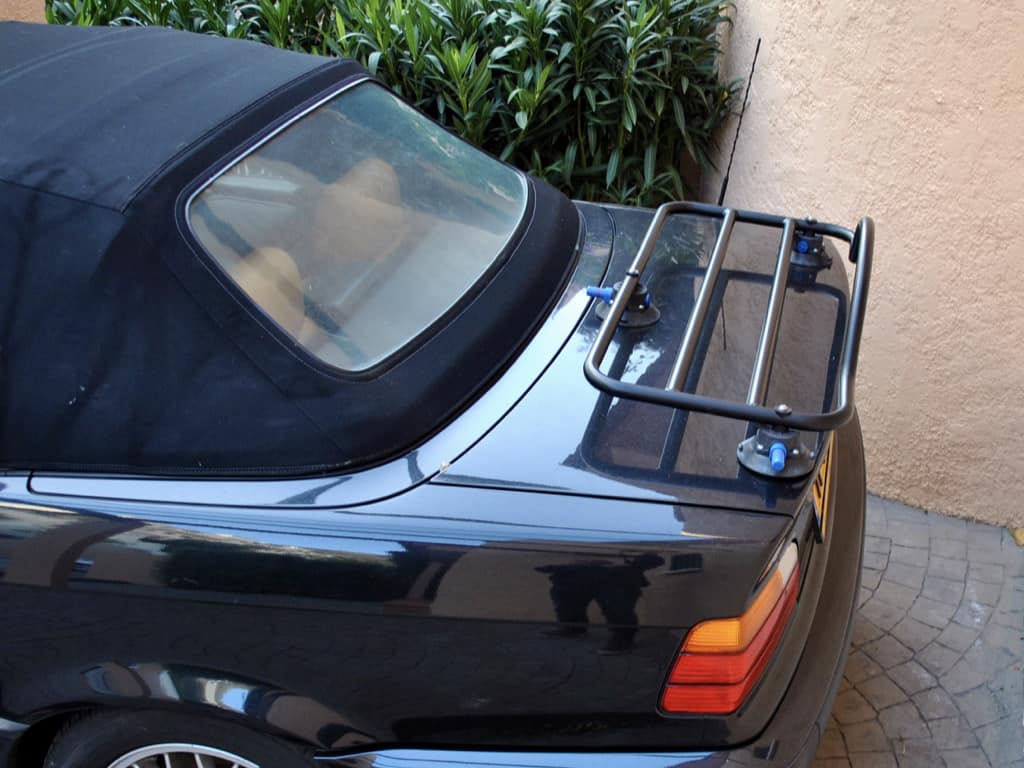 black bmw 3 series convertible e36 mode with the hood up and a black luggage rack fitted