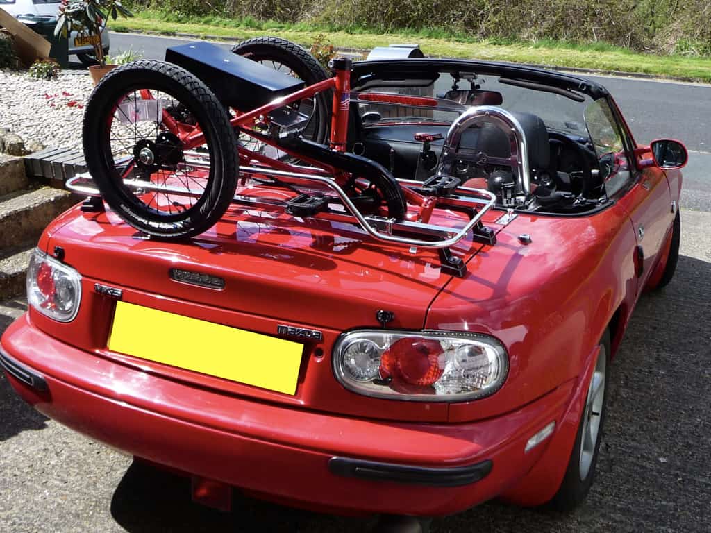 red mazda mx5 mk1 with a stainless steel luggage rack fitted carrying a bike