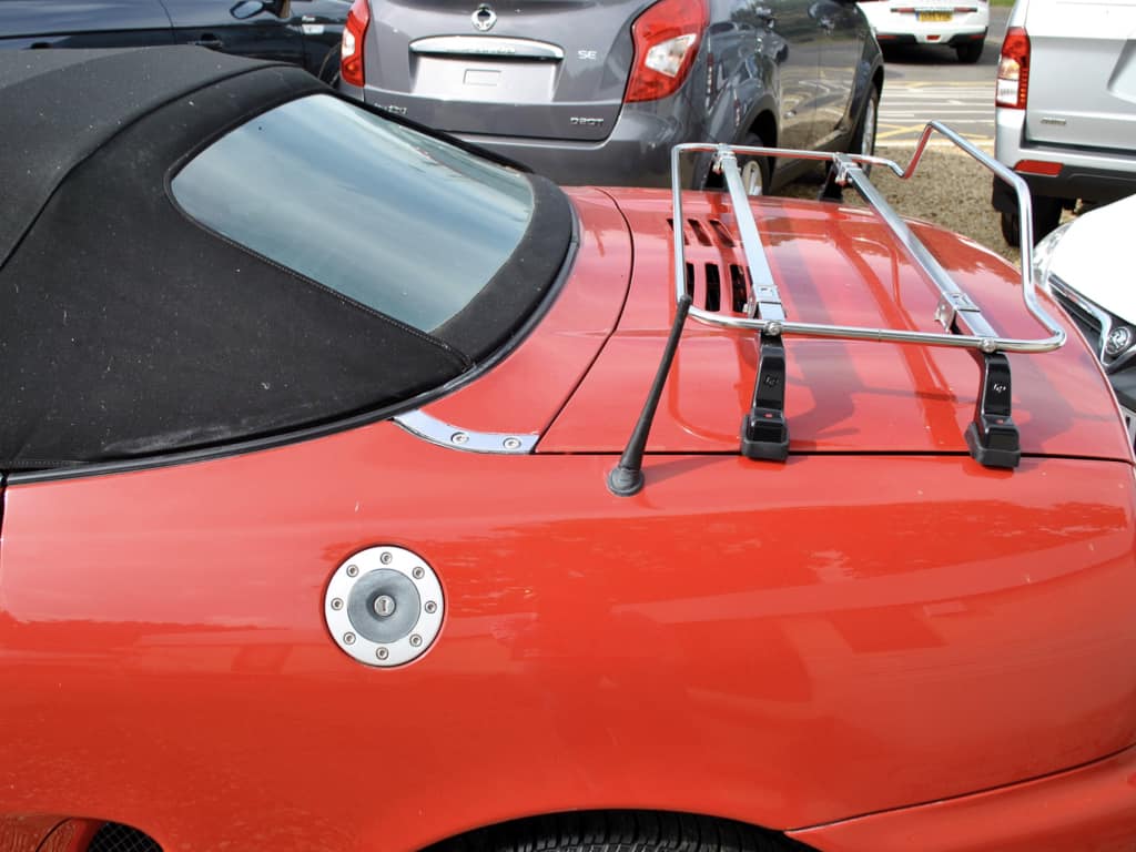 Side view of a stainless steel luggage rack fitted to a red MGTF