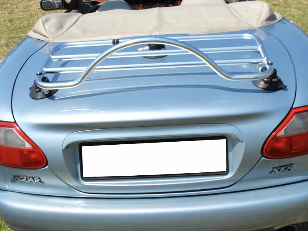 rear view of a jaguar xk8 convertible with the hood down in a field with a chrome luggage rack fitted