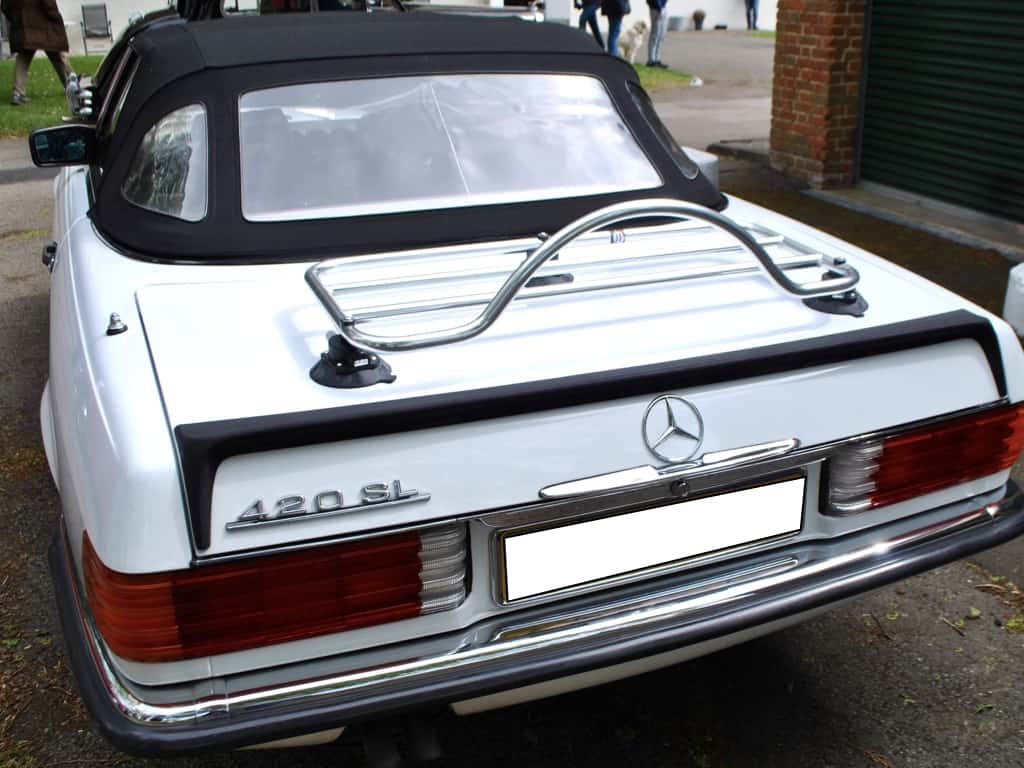 white mercedes benz sl r107 420 with a rear rubber spoiler and a luggage rack fitted