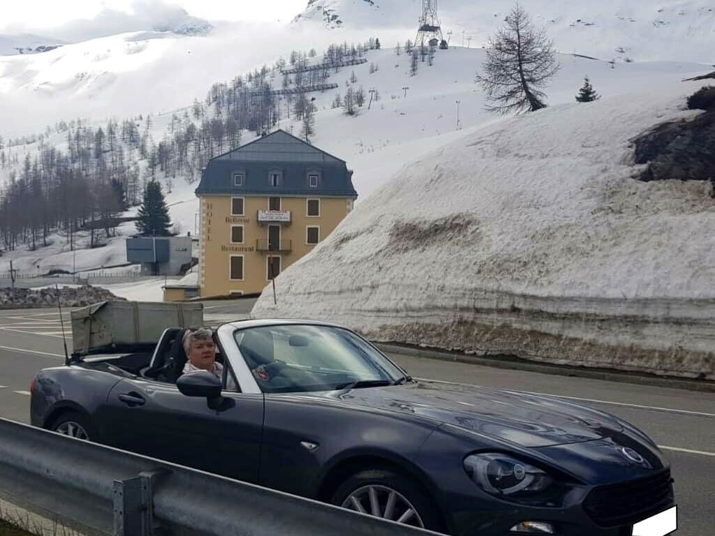dark grey fiat 124 spider with the hood down and a revo-rack luggage rack and trunk fitted to the boot in the Austrian alps