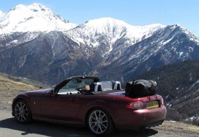 red mx5 mk3 with a bot-bag original luggage rack fitted in the alps with mountains in the background.