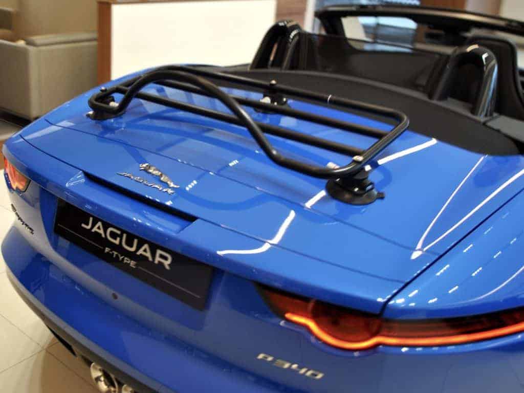 blue jagaur f type p340 convertible with the hood down in a jaguar garage and a black luggage rack fitted 