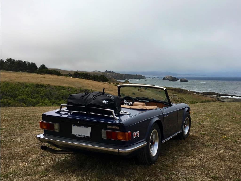 blue triumph tr6 on a cliff looking out to sea with a boot-bag vacation luggage rack fitted