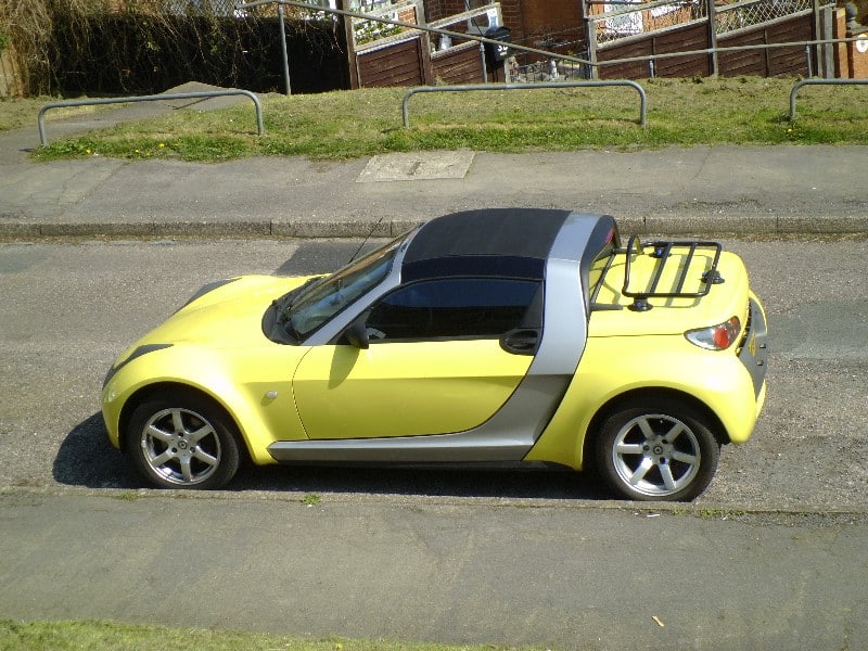 yellow smart roadster with a black luggage rack fitted in a suburban setting on the street