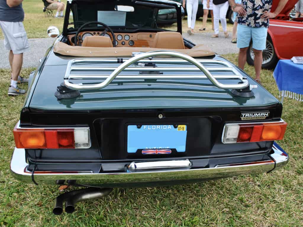 green triumph tr6 with a tan interior and a stainless steel luggage rack fitted hood down at a car show