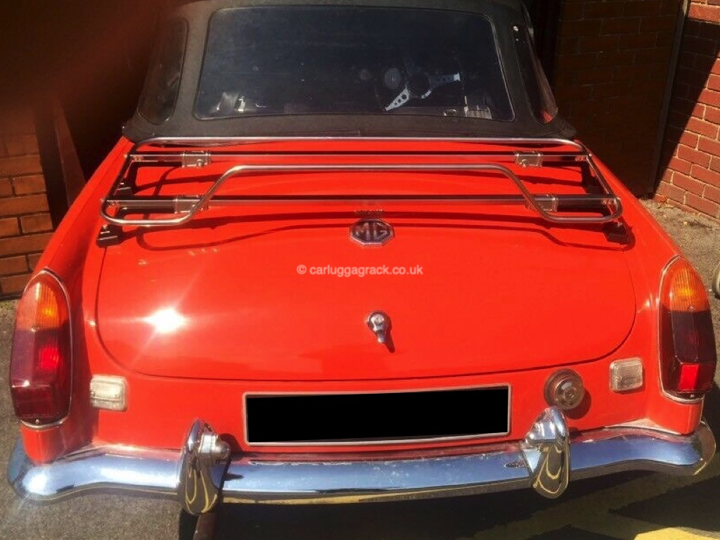 bright orange mgb with a stainless steel luggage rack fitted on a sunny day outside a garage