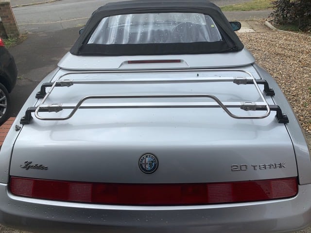 silver alfa spider convertible with a stainless steel luggage rack fitted on a driveway