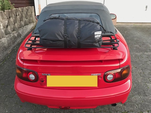 red mazda mx5 mk1 with a black luggage rack fitted carrying a black bag