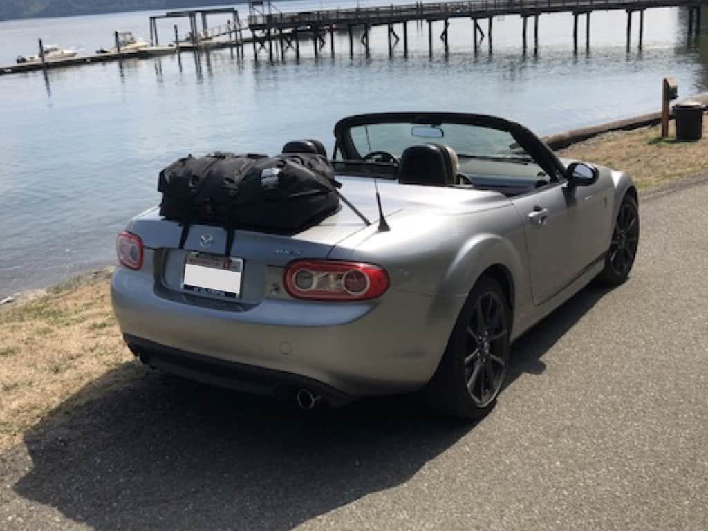 silver mazda mx5 roadster coupe next to a lake with a boot-bag luggage rack fitted hood down