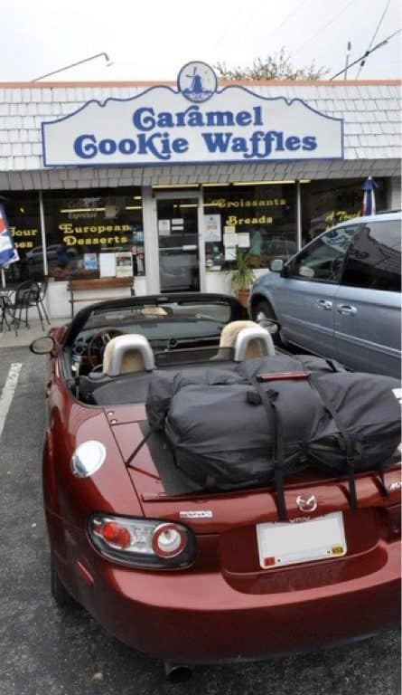 a burgancy mazda mx5 mk3 miata nc outside a bakers with a boot-bag vacation luggage rack fitted