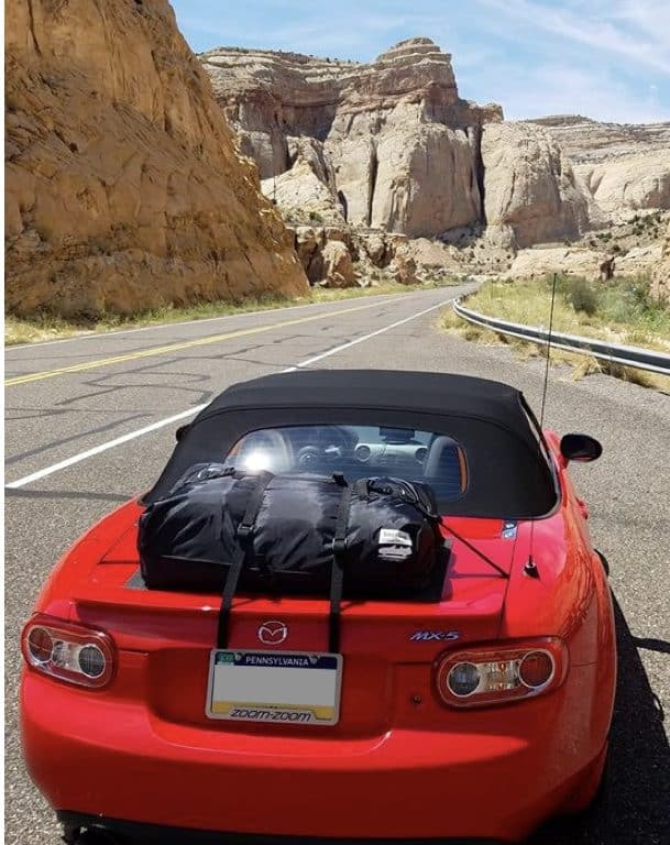 red mazda mx5 mk2 miata nb with a boot-bag original luggage rack fitted on a canyon road 