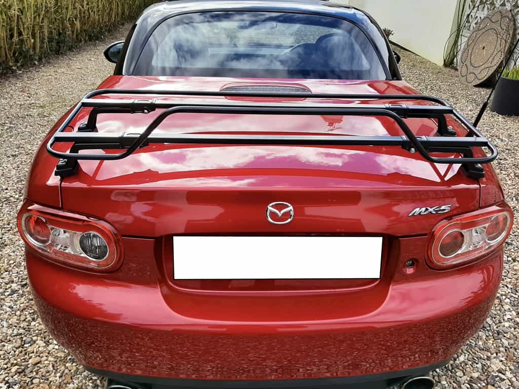 rear view of a mazda mx5 roadster coupe in burgandy with a black roof and with a black luggage rack fitted
