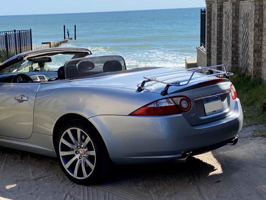 Grey Jaguar XK convertible with a stainless steel luggage rack fitted next to a beach