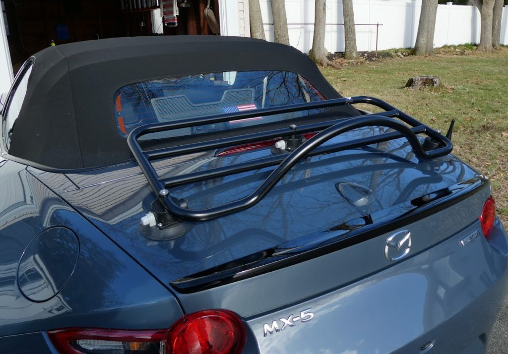 blue mazda mx5 mk4 with a black luggage rack fitted photographed from the rear outside a white house