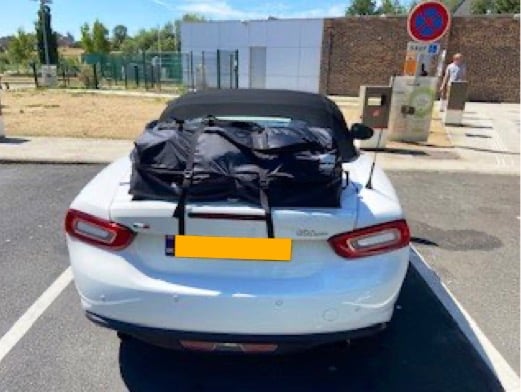white fiat 124 spider in a car park with a boot-bag vacation luggage rack fitted photographed from the rear