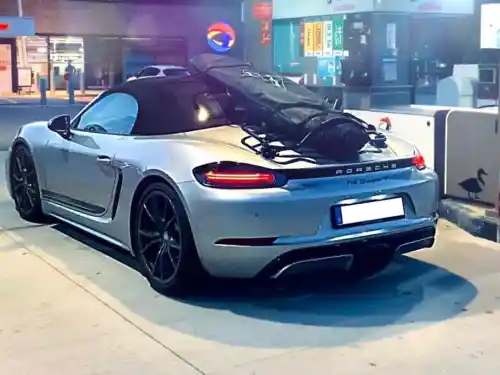 silver porsche boxster 718 in a petrol station at night with a revo-rack luggage rack fitted carrying a surf board