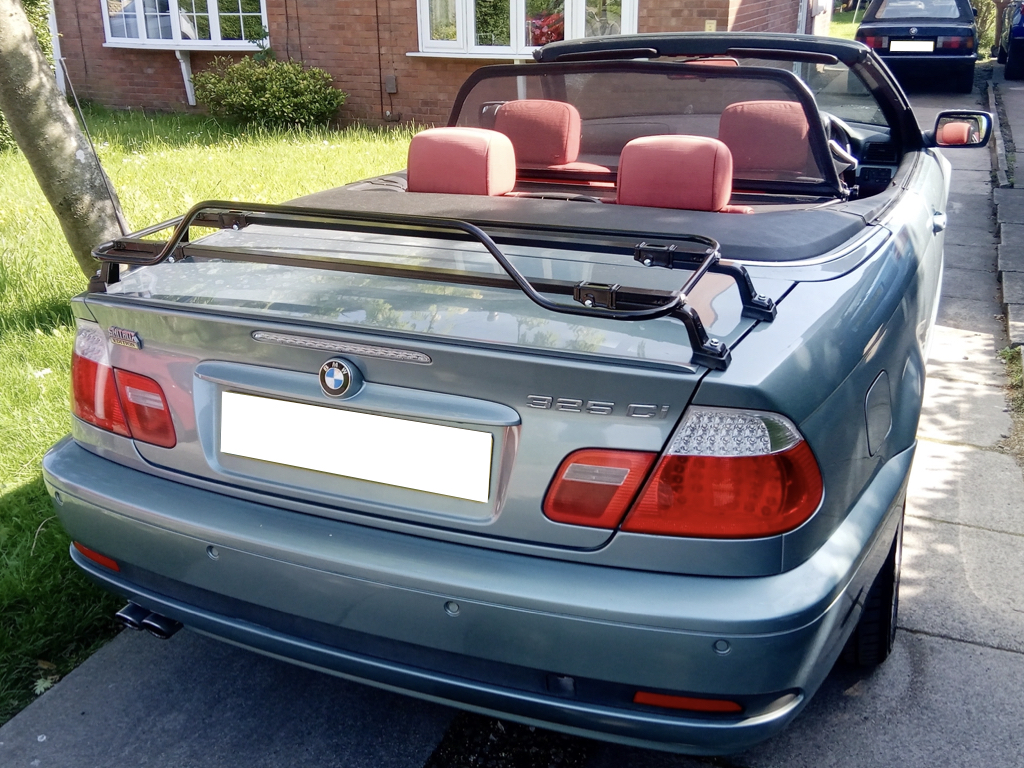 silver bmw 325ci e46 convertible roof down on a driveway with a black luggage rack fitted photographed from the rear on a sunny day