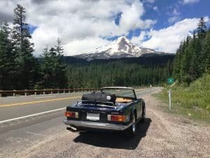 Blue Triumph TR6 with hood down with luggage carrier attached looking at the mountains