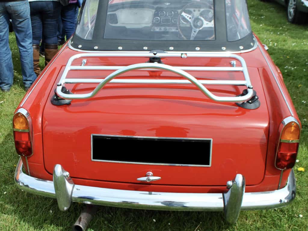 Rear view of Red Triumph TR5 with black hood with stainless steel luggage rack attached at car show