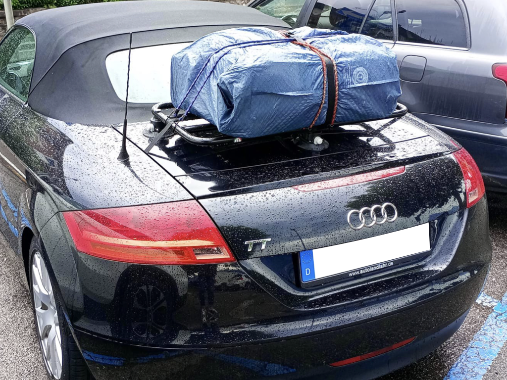 black audi tt roadster with a luggage rack fitted carrying a blue suitcase photographed from the rear in the rain