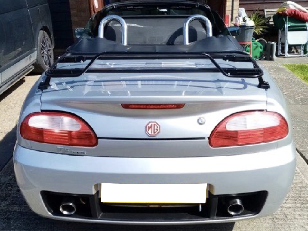 silver mgf with a black luggage rack fitted photographed from the rear outside a garage roof down in the sunshine