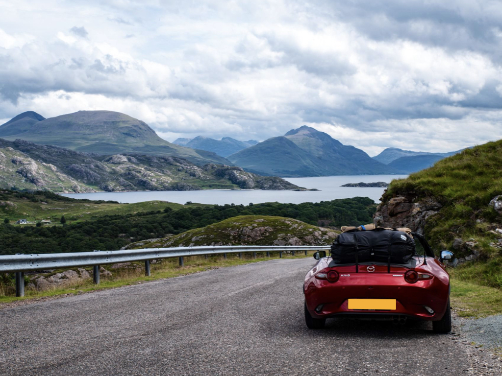burgandy mazda mx5 nd mk4 with a boot-abg luggage rack fitted to the boot, photographed from the rear on a mountain road in scotland ovrelooking a loch
