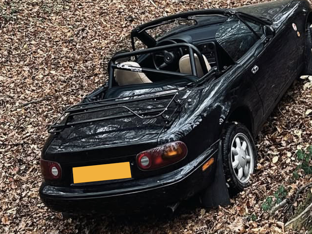black Mazda mx5 na mk1 with a luggage rack fitted  photographed from above hood down on autumn leaves 